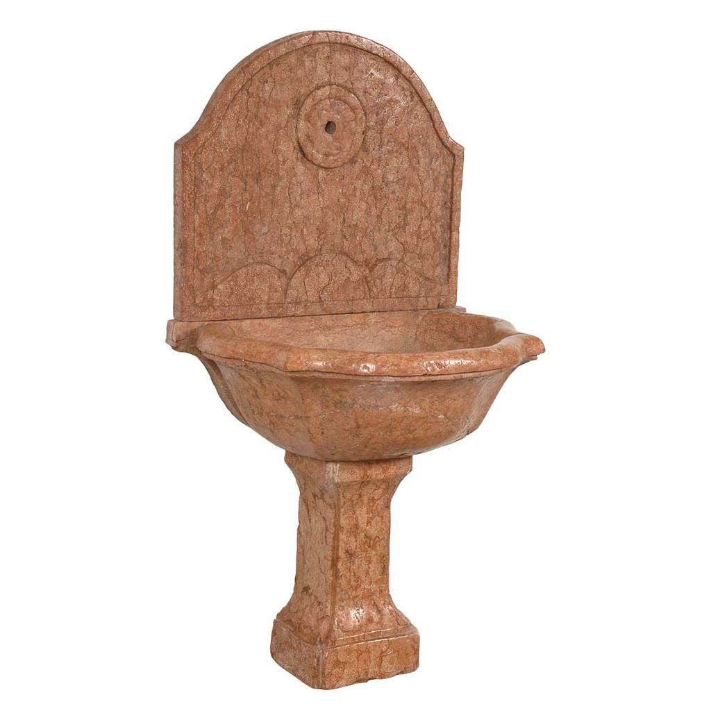 A 17th century marble font with arched backsplat on a pedestal base. View 1